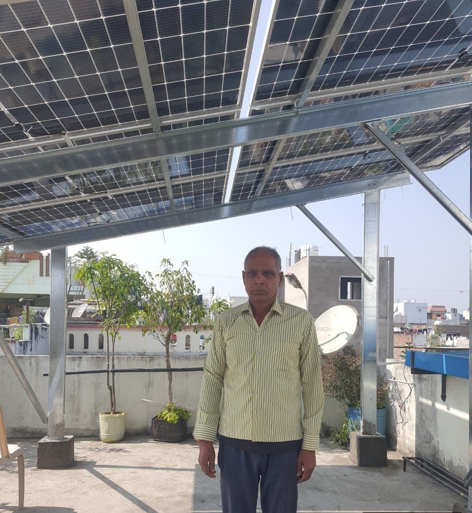 Homeowner standing under an elevated rooftop solar system installed by Genius Solar in Mukherjee Nagar, Indore