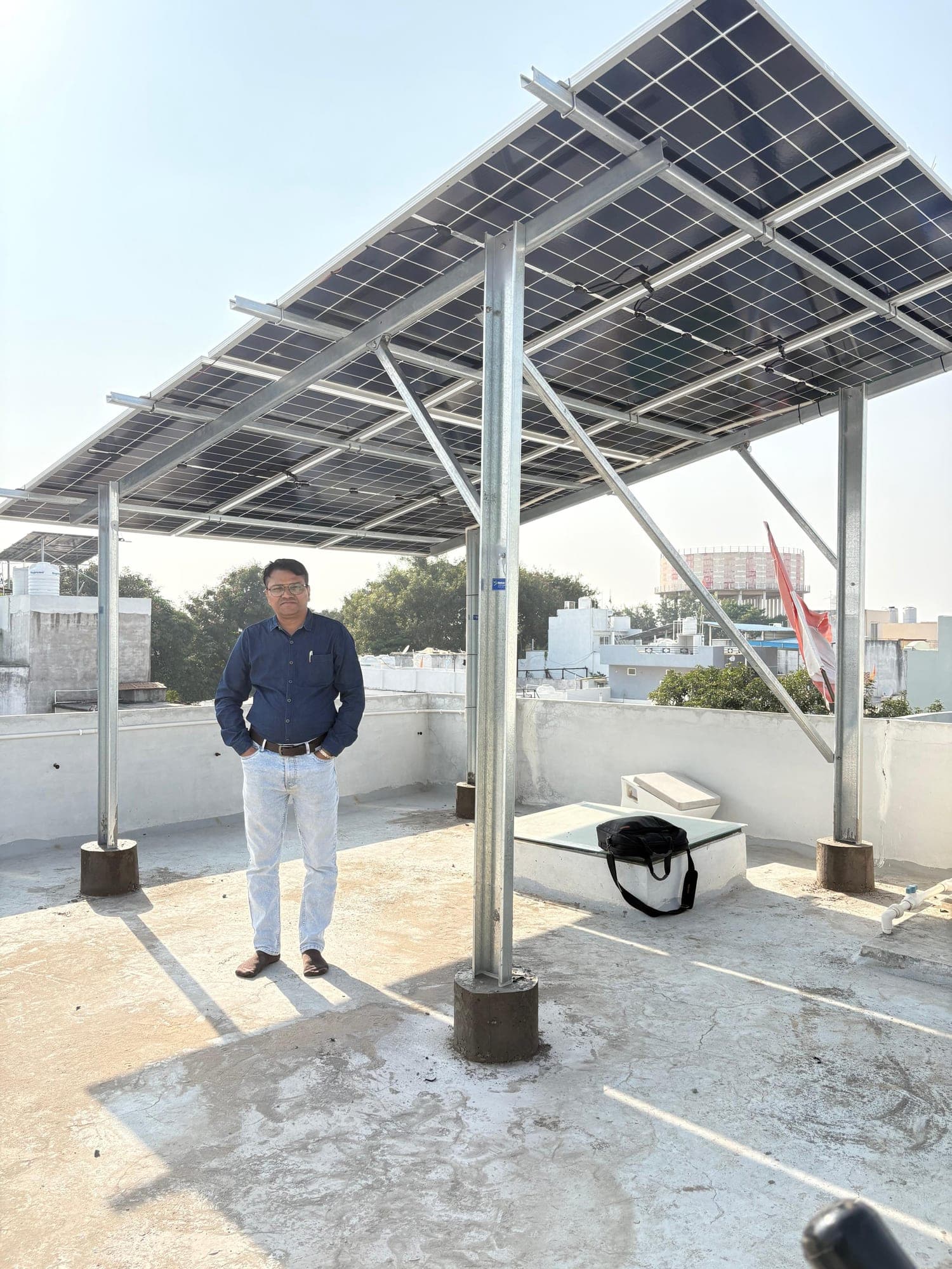 Owner under a tilted elevated solar array on an Indore terrace, November 2025