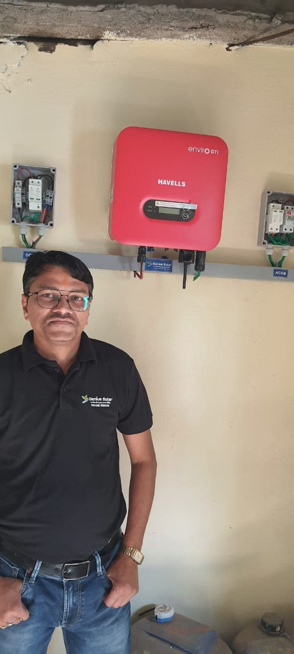 Genius Solar team member beside a wall-mounted solar inverter and AC distribution box in Indore